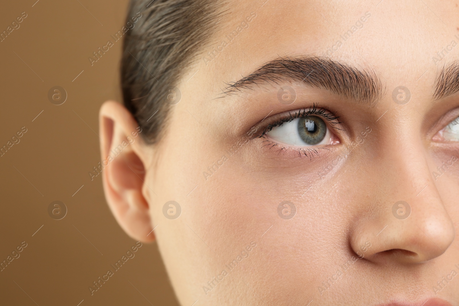 Photo of Young woman with perfect eyebrows on brown background, closeup. Space for text