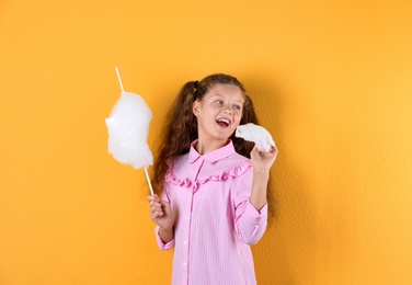 Little girl with cotton candy on color background