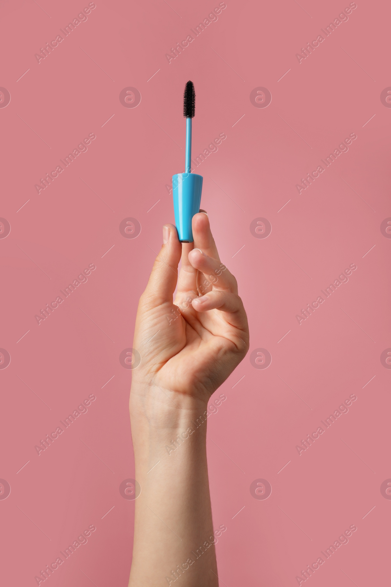 Photo of Woman holding mascara for eyelashes on dusty rose background, closeup