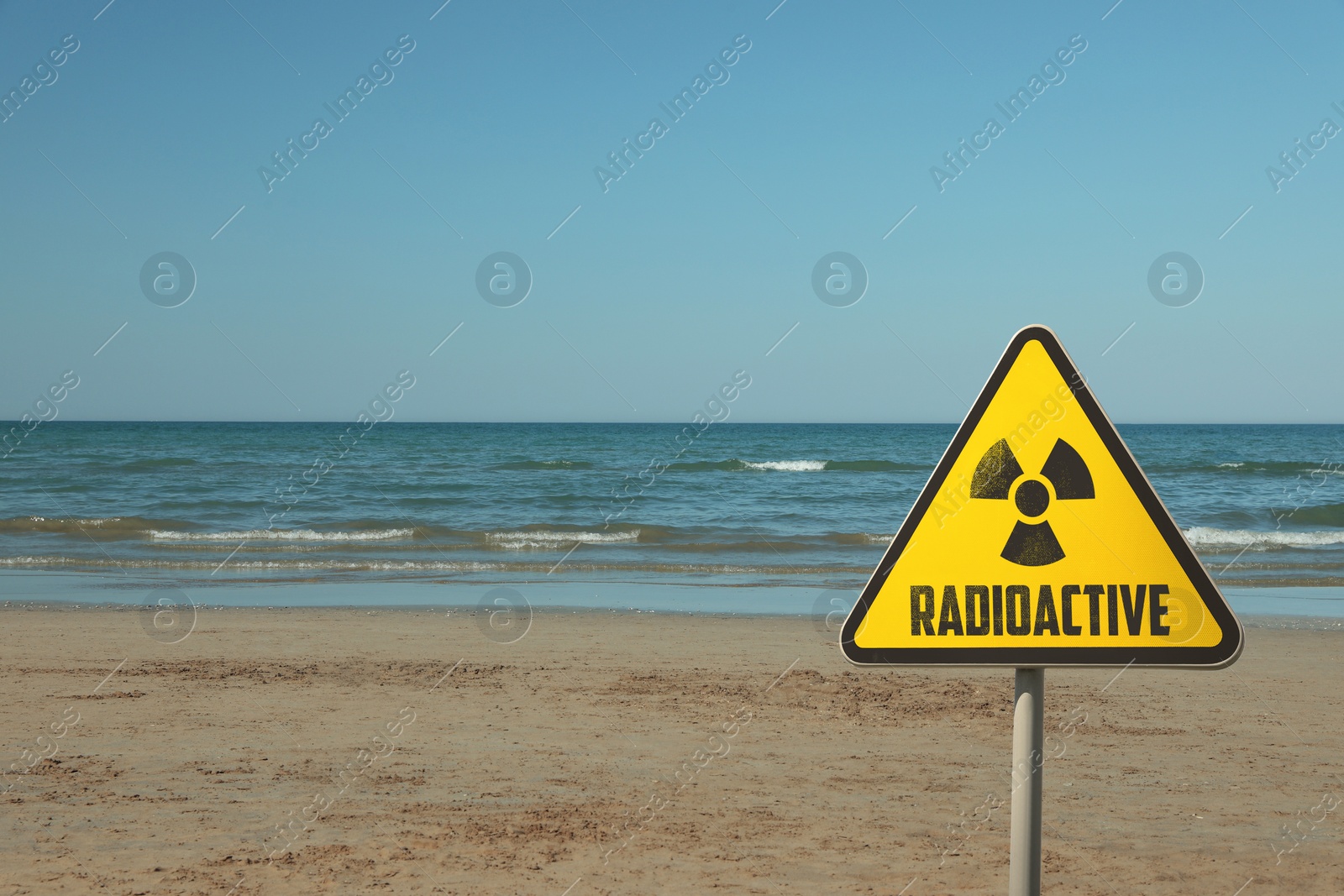 Image of Radioactive pollution. Yellow warning sign with hazard symbol near contaminated area on beach. Space for text