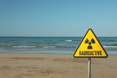 Image of Radioactive pollution. Yellow warning sign with hazard symbol near contaminated area on beach. Space for text