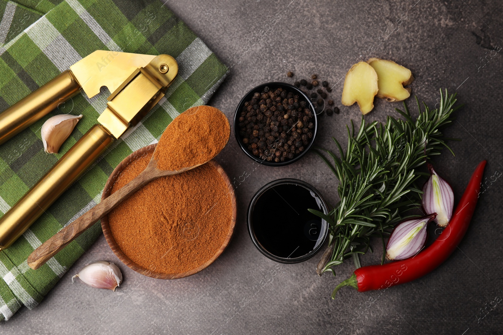 Photo of Aromatic spices, fresh ingredients for marinade and garlic press on brown table, flat lay