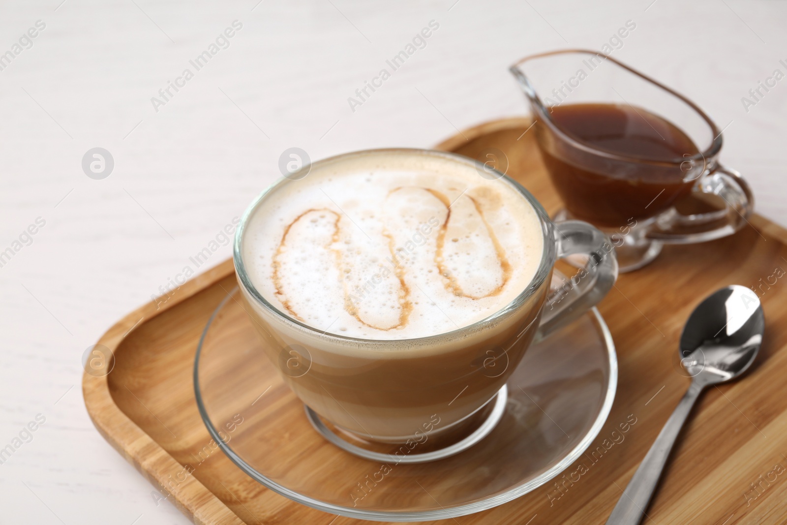 Photo of Tray with tasty caramel macchiato, spoon and syrup on table