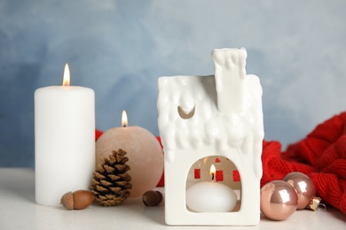 Composition with candle in house shaped holder on white wooden table. Christmas decoration