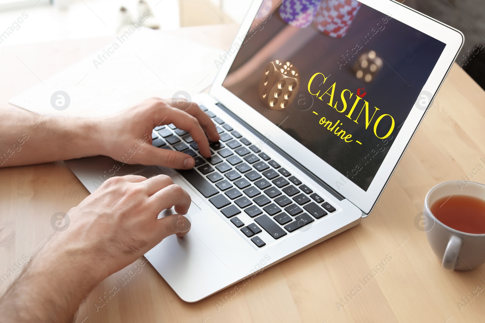 Image of Man playing poker on laptop at wooden table, closeup. Casino online