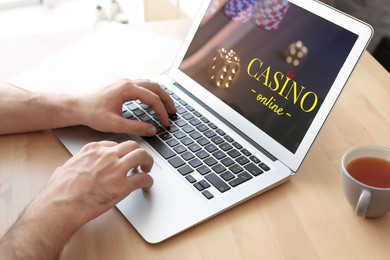 Image of Man playing poker on laptop at wooden table, closeup. Casino online