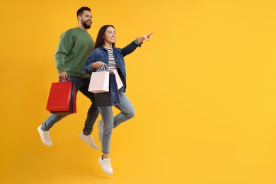 Photo of Happy couple with shopping bags jumping on orange background. Space for text