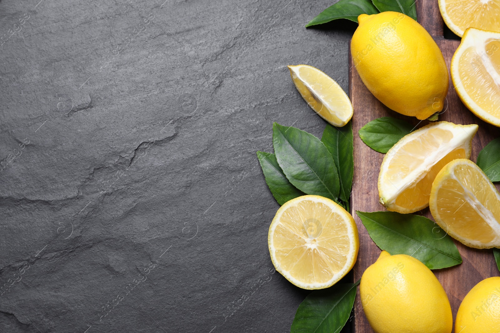 Photo of Many fresh ripe lemons with green leaves on black table, top view. Space for text