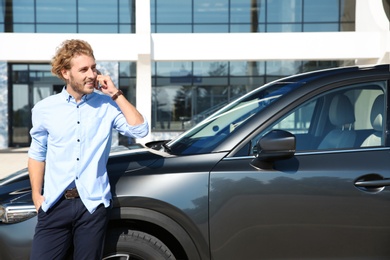 Photo of Young man talking on phone near modern car, outdoors