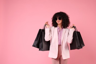 Photo of Happy young woman with shopping bags and stylish sunglasses on pink background. Space for text