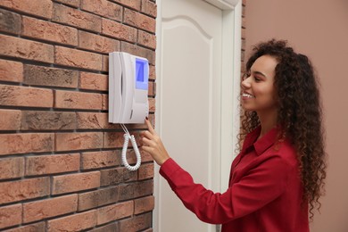 Photo of Young African-American woman pressing button on intercom panel indoors