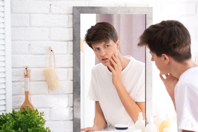 Teenage boy with acne problem looking in mirror at home