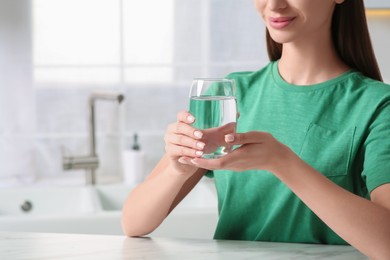 Healthy habit. Woman holding glass with fresh water in kitchen, closeup. Space for text