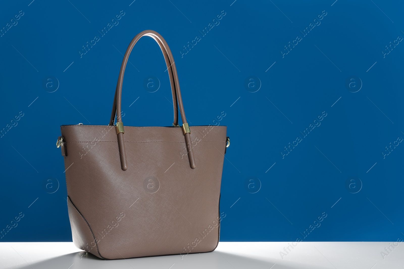 Photo of Stylish woman's bag on white table against blue background. Space for text