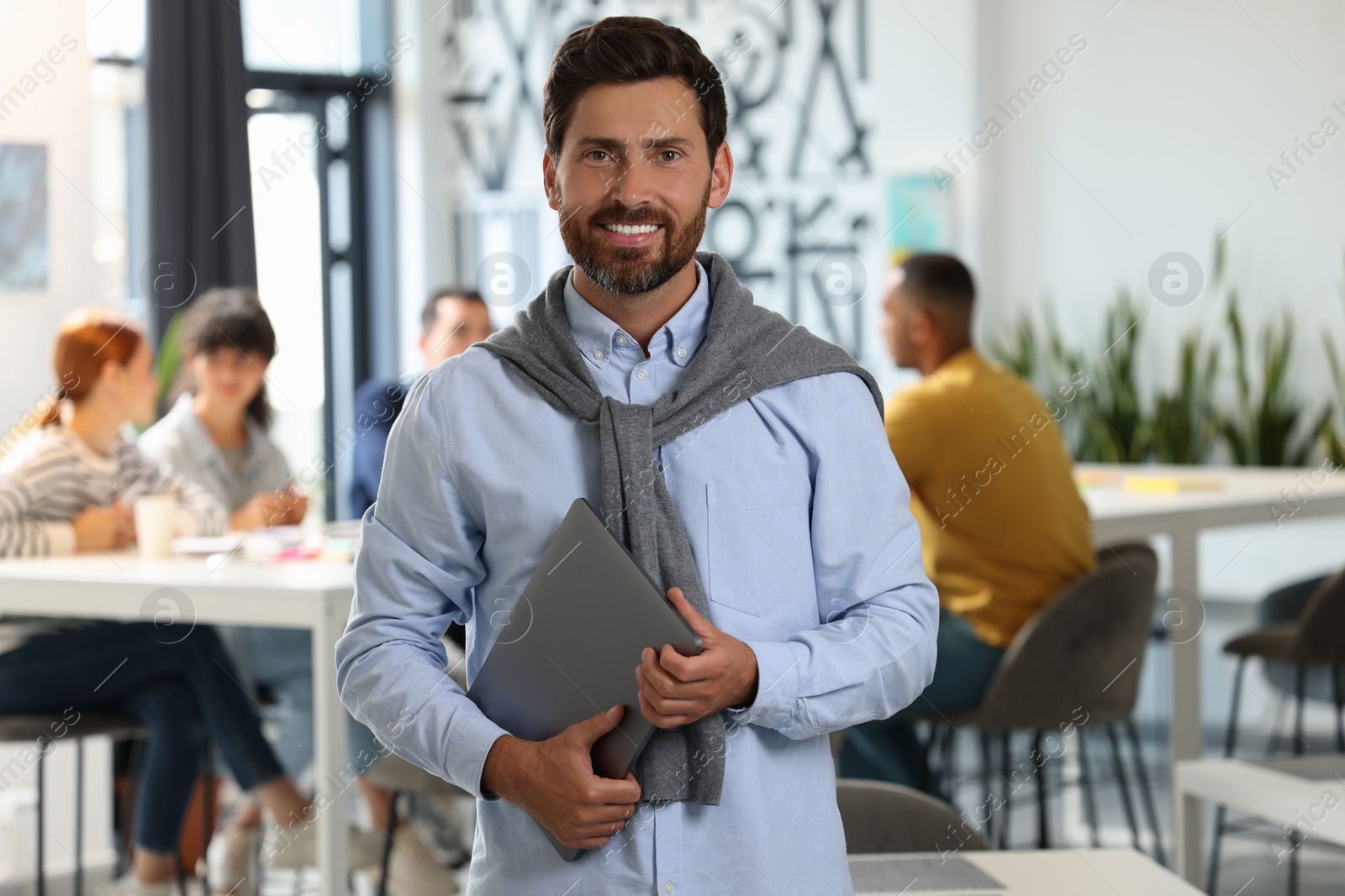 Photo of Team of employees working together in office. Happy man with laptop indoors