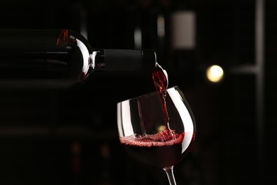 Photo of Pouring red wine from bottle into glass on blurred background, closeup