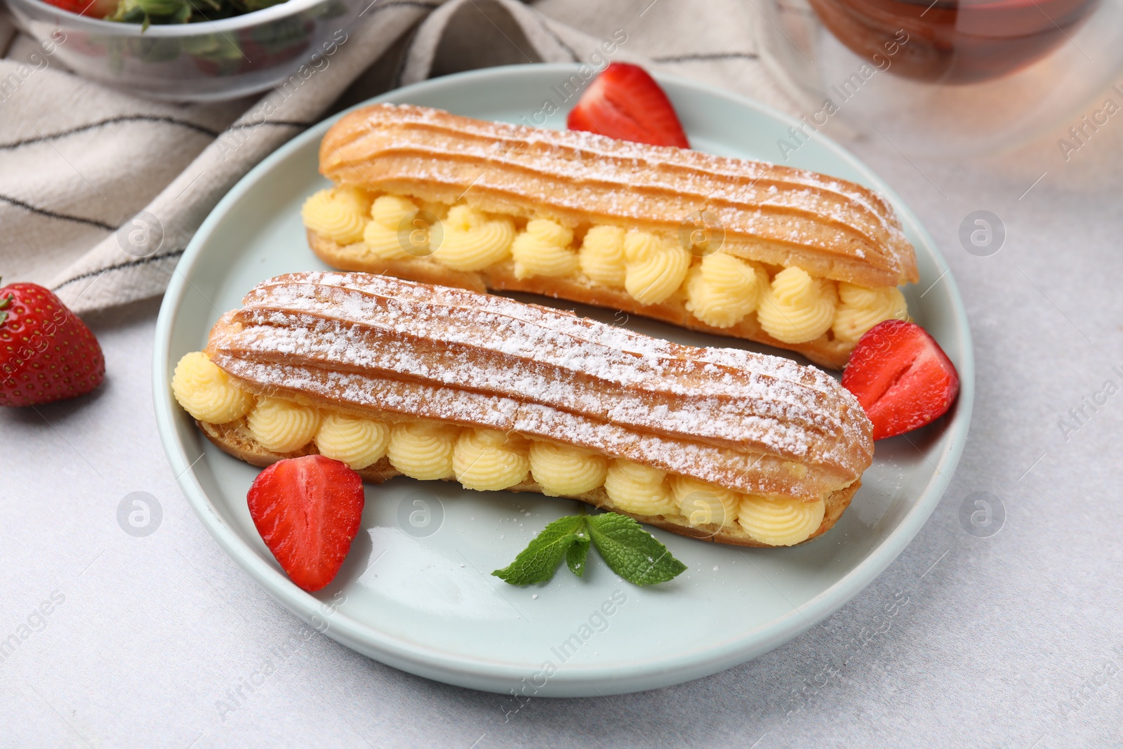 Photo of Delicious eclairs filled with cream, strawberries and mint on light table