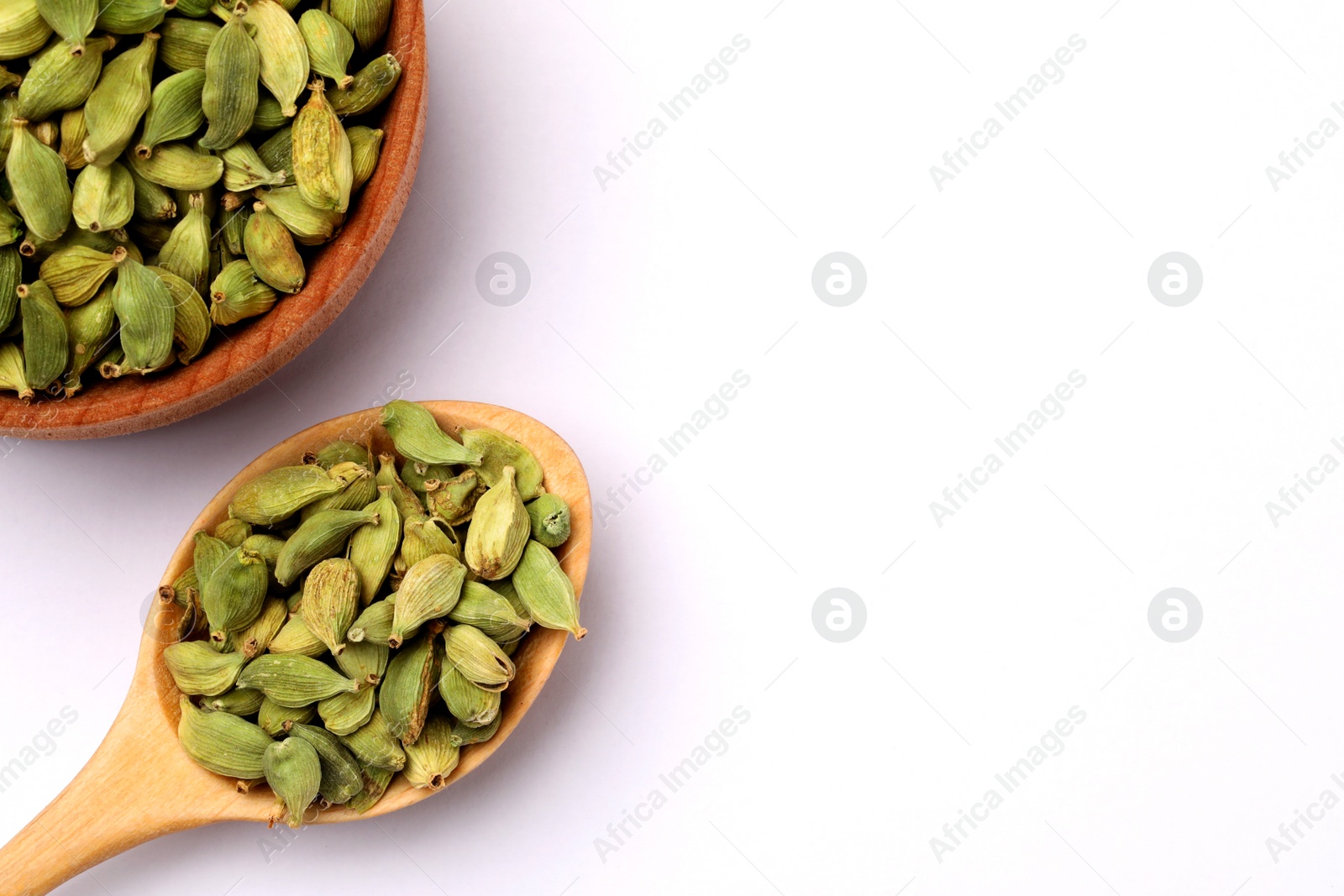 Photo of Wooden bowl and spoon with cardamom on white background, flat lay. Space for text