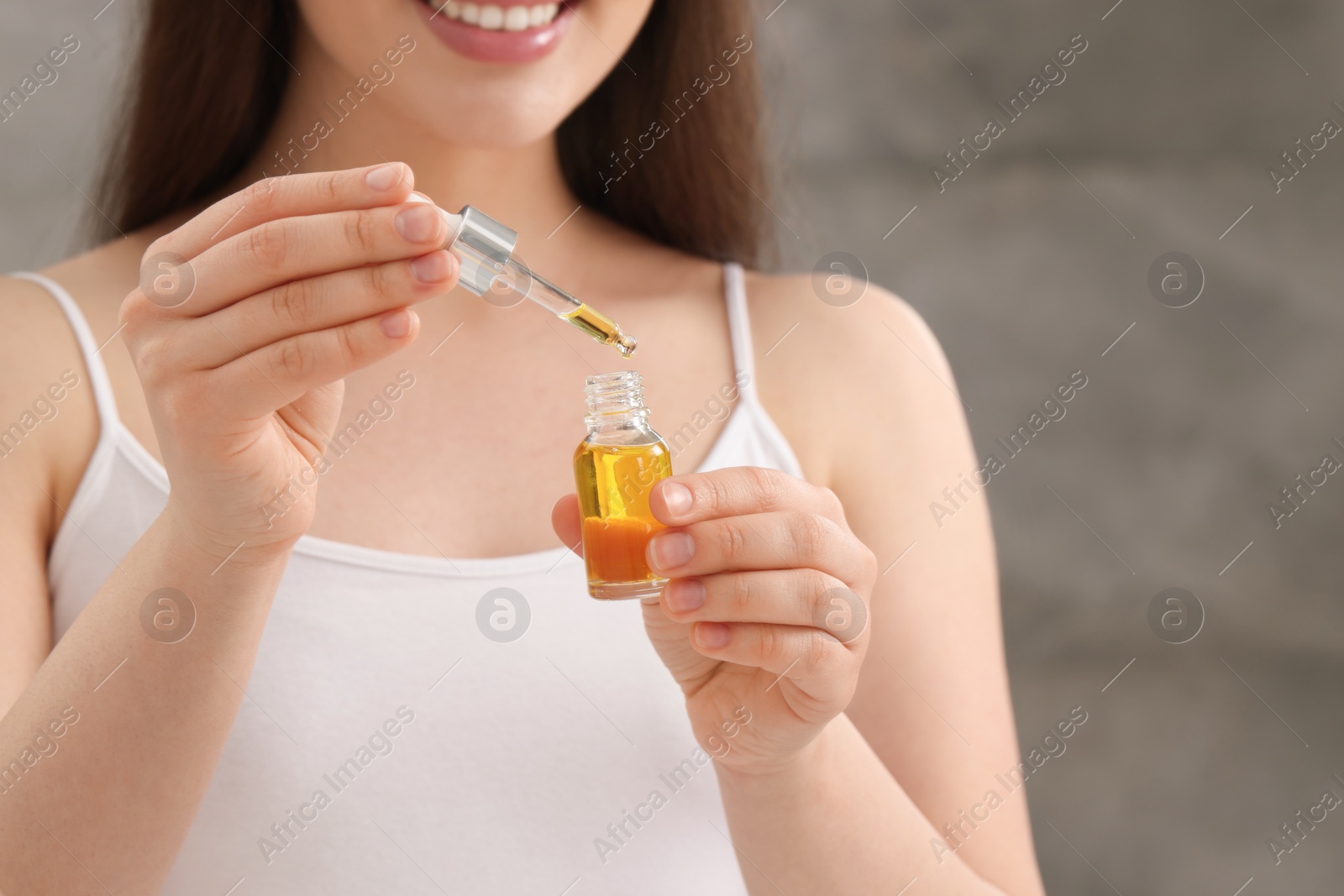 Photo of Woman with bottle of essential oil on blurred background, closeup