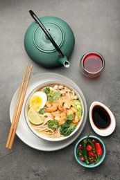 Photo of Delicious ramen with shrimps and egg in bowl served on grey table, flat lay. Noodle soup