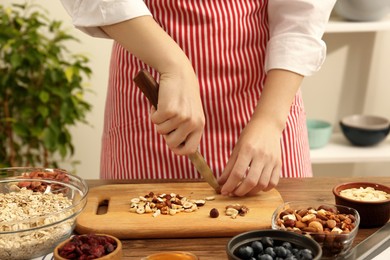 Making granola. Woman cutting nuts at table in kitchen, closeup