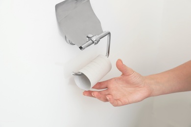 Photo of Woman reaching holder with empty toilet paper roll, closeup