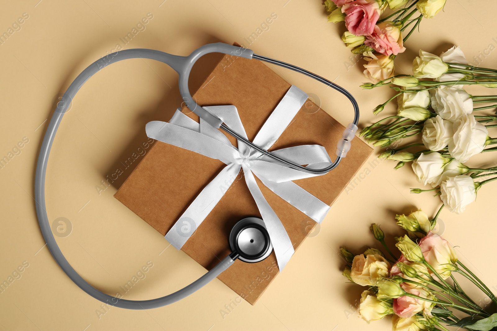 Photo of Stethoscope, gift box and flowers on beige background, flat lay. Happy Doctor's Day