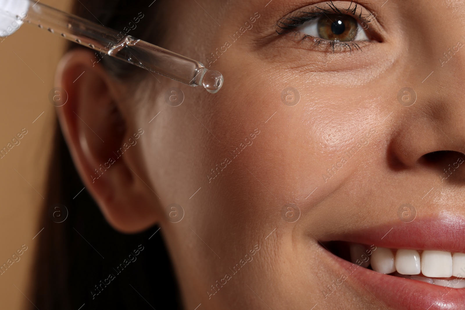 Photo of Beautiful young woman applying serum onto her face on beige background, closeup