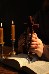 Woman praying at table with burning candles and Bible, closeup