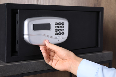 Photo of Woman opening black steel safe with electronic lock, closeup