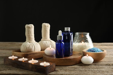 Photo of Spa composition. Cosmetic products, herbal bags, burning candles and sea salt on wooden table against black background