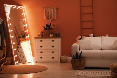 Large mirror with light bulbs and chest of drawers in stylish room interior