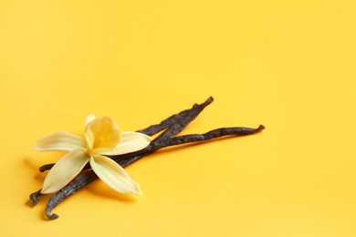 Photo of Vanilla sticks and flower on yellow background. Space for text