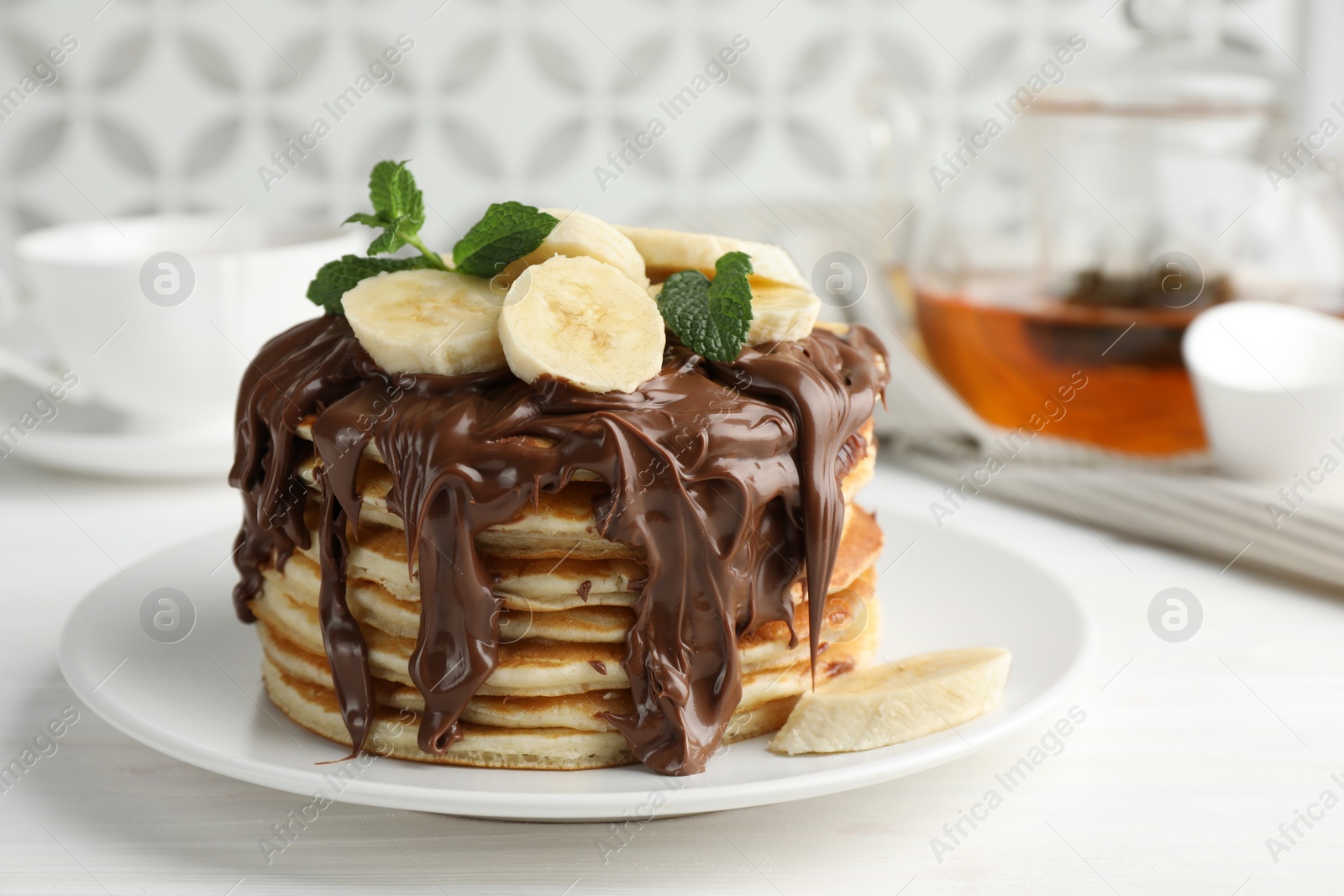 Photo of Tasty pancakes with chocolate spread, sliced banana and mint on white wooden table, closeup