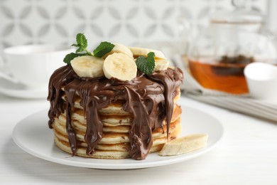 Photo of Tasty pancakes with chocolate spread, sliced banana and mint on white wooden table, closeup