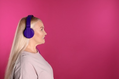 Mature woman enjoying music in headphones on color background. Space for text