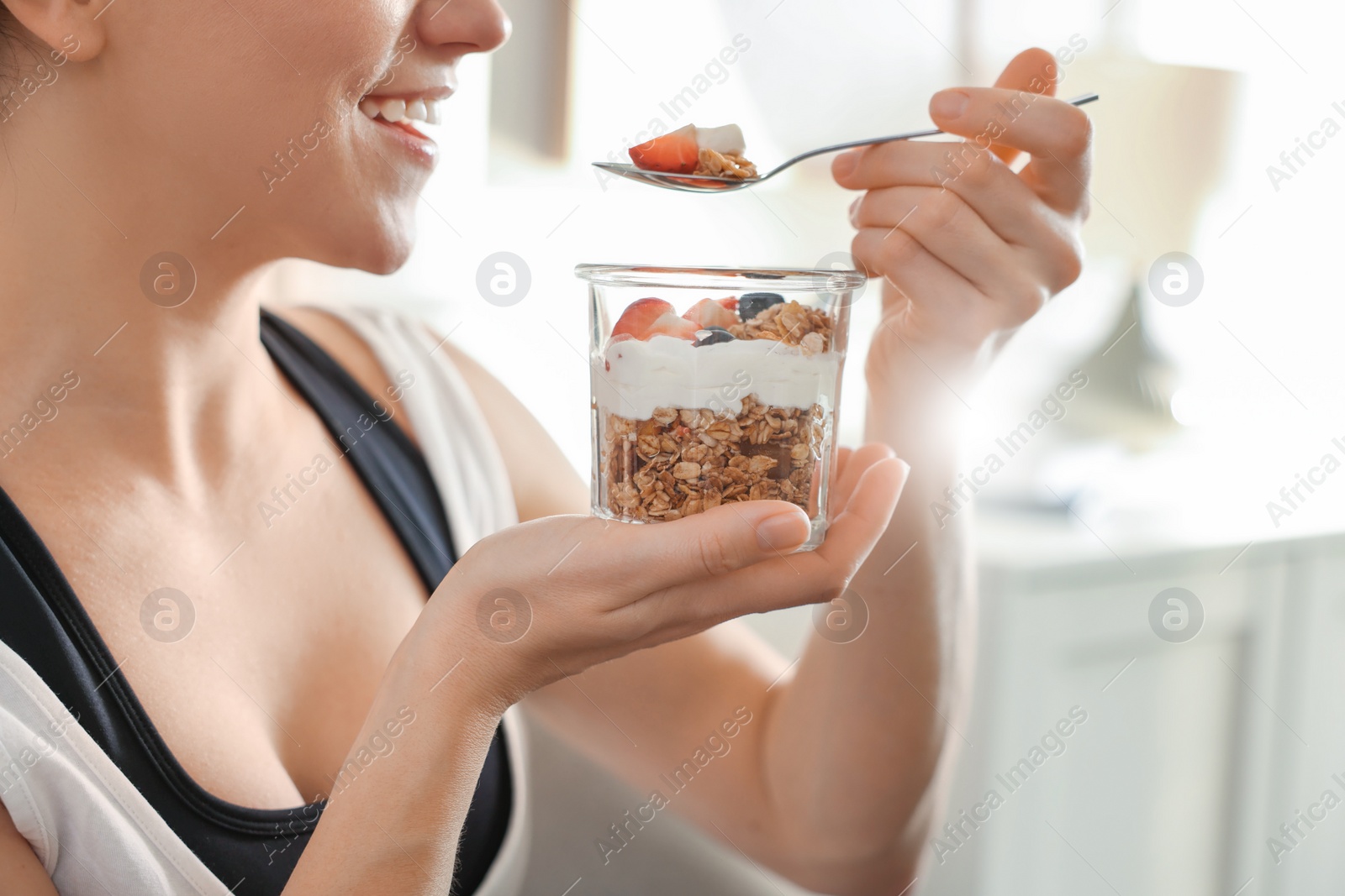 Photo of Woman eating tasty granola with fresh berries and yogurt at home, closeup