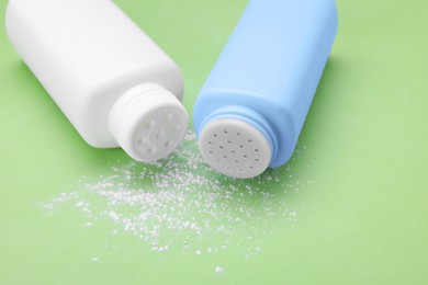 Photo of Bottles and scattered dusting powder on light green background. Baby cosmetic products