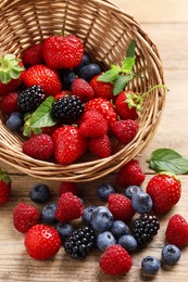 Photo of Wicker basket with many different fresh ripe berries on wooden table