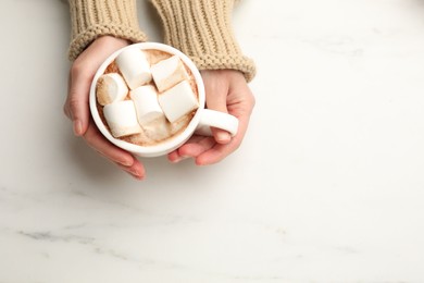 Photo of Woman with cup of tasty hot chocolate and marshmallows at white marble table, top view. Space for text