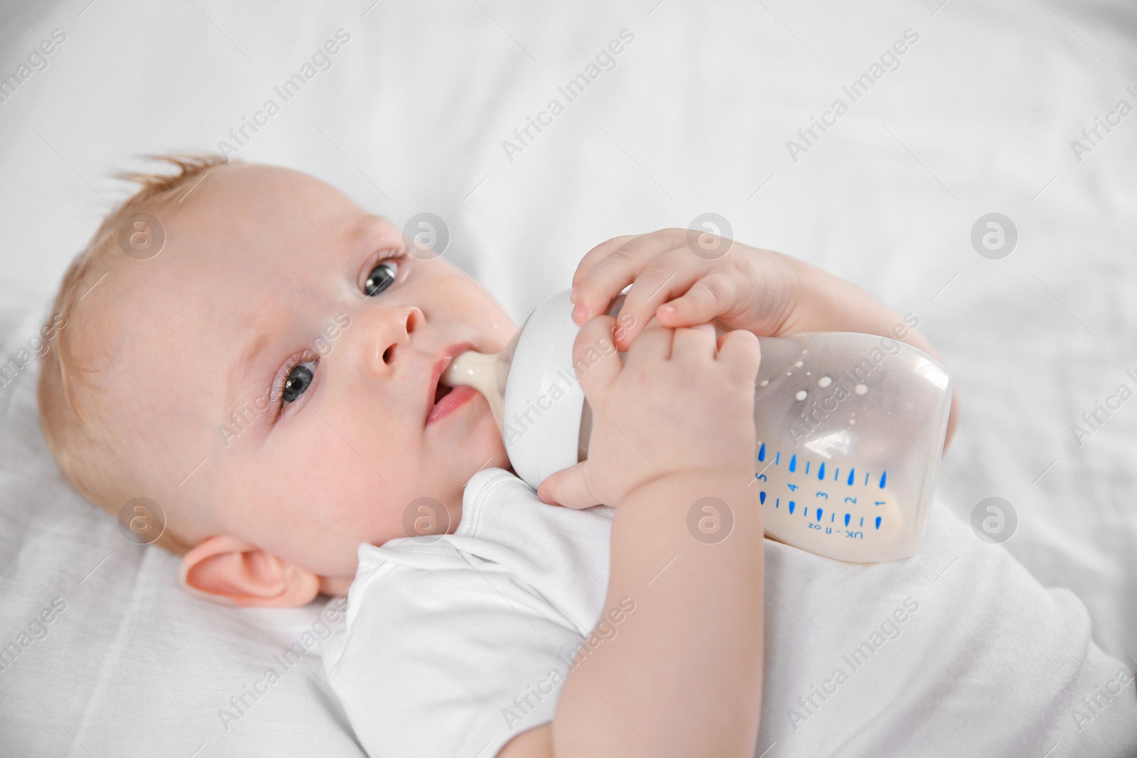 Photo of Baby drinking milk from bottle on bed, closeup