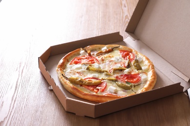 Photo of Cardboard box with tasty pizza on wooden table