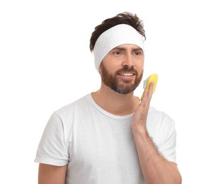 Man with headband washing his face using sponge on white background