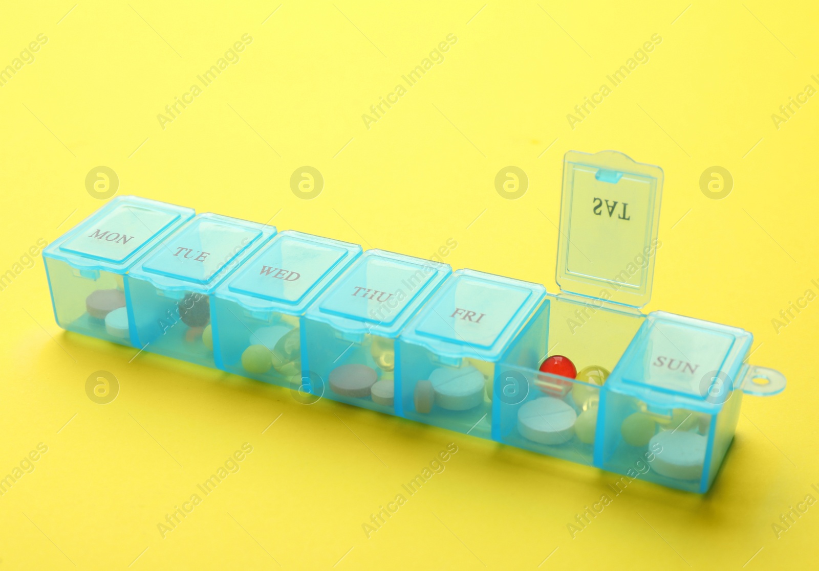 Photo of Plastic box with different pills on yellow background