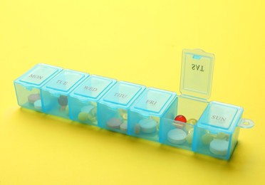 Photo of Plastic box with different pills on yellow background