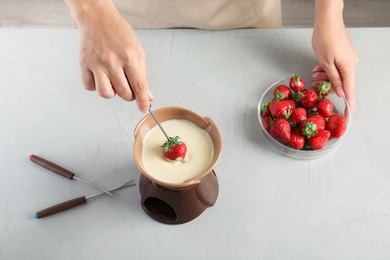 Photo of Woman dipping ripe strawberry into bowl with white chocolate fondue on table