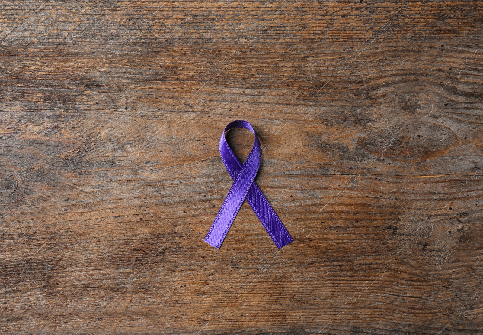 Photo of Purple ribbon on brown wooden background, top view. Domestic violence awareness