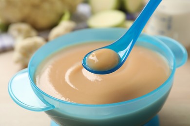 Spoon of healthy baby food over bowl on table, closeup