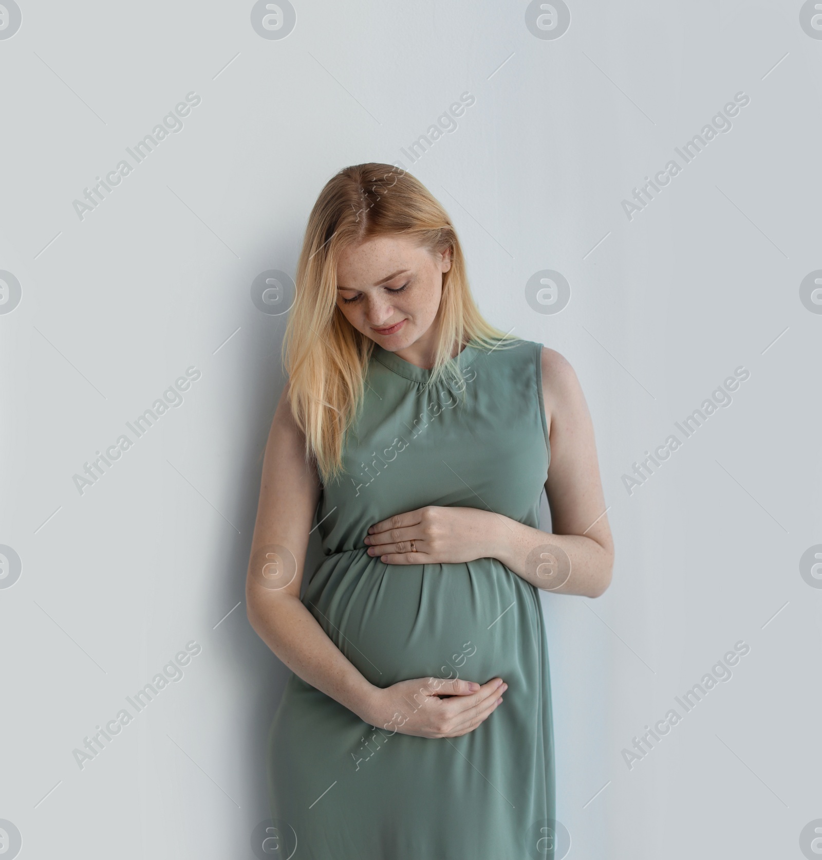 Photo of Young pregnant woman touching belly on light background