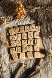Photo of Many wooden runes and dried flowers on fur, flat lay